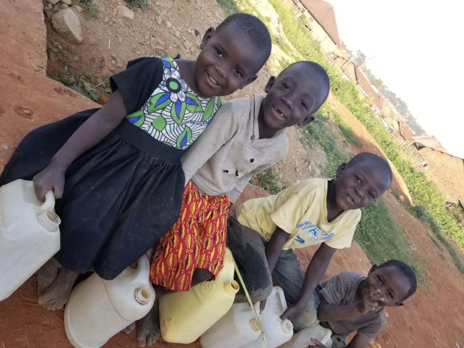 Four children sitting with water jerry cans they use to fetch water instead of attending school