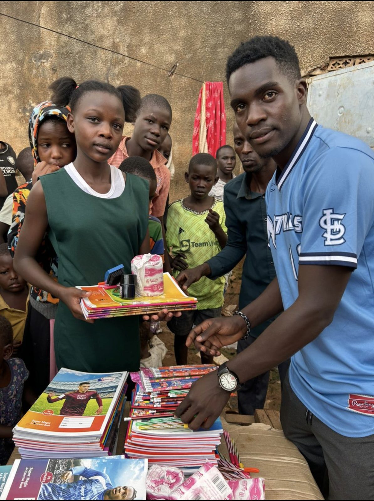 Angello and a volunteer handing out notebooks, pencils, and school supplies to children in Uganda