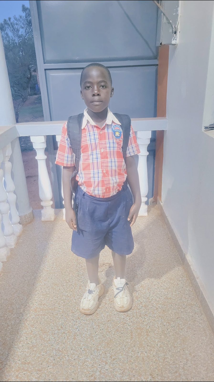 A boy in a school uniform and backpack standing on a school walkway