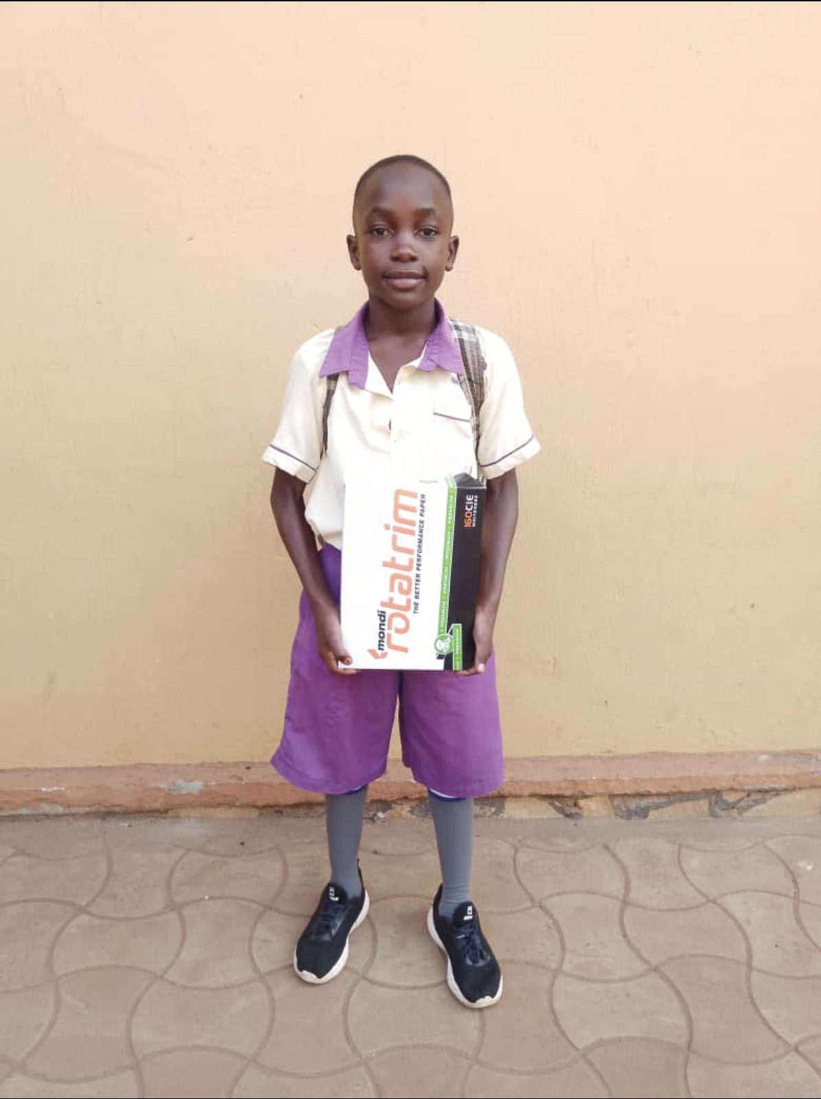 A boy in school uniform holding a pack of exercise books