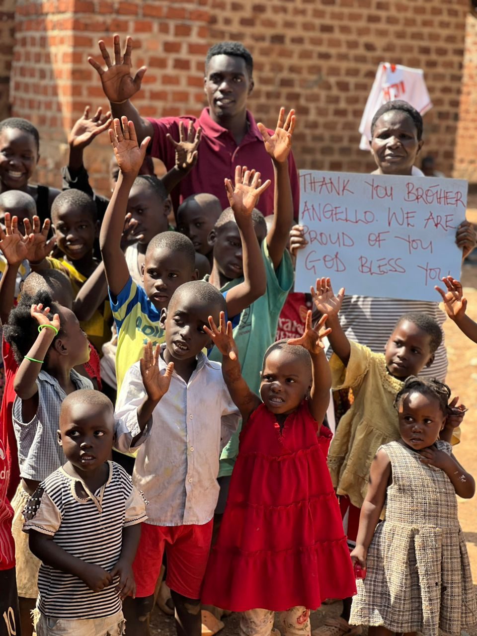 A group of children and a mother waving and holding a sign that reads Thank You Brother Angello, We Are Proud of You, God Bless You