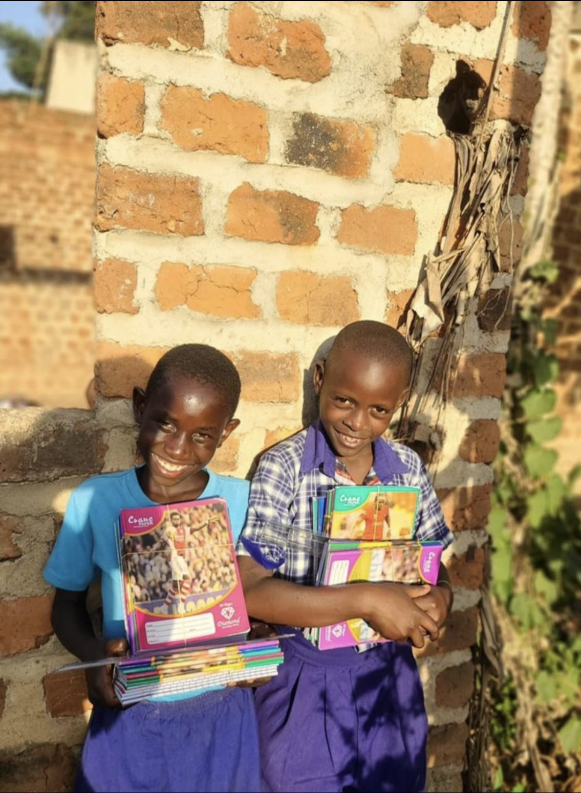Two smiling boys holding stacks of new notebooks and pencils